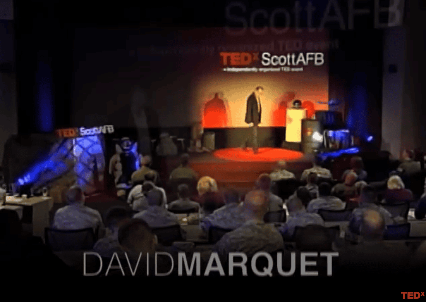 Former US Navy Captain David Marquet presenting on stage at a TEDx ScottAFB event, talking about building leadership capability rather than followers.