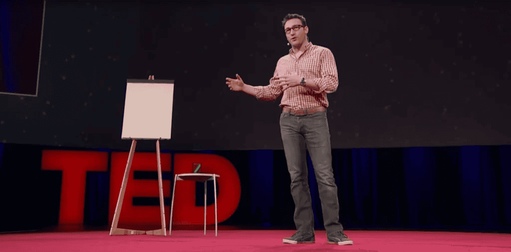 Simon Sinek presenting his iconic Start With Why talk on the red TED stage, gesturing next to an easel and flipchart.