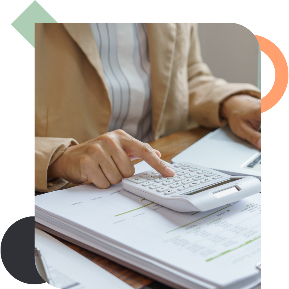 Close-up of a person in a beige blazer using a white desk calculator over a stack of printed financial charts and data reports, illustrating the process of tracking execution and analyzing business impact.